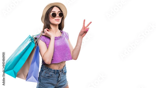 Fototapeta Full length portrait of a happy excited girl in bright colorful clothes holding shopping bags while standing and showing peace gesture isolated over white background