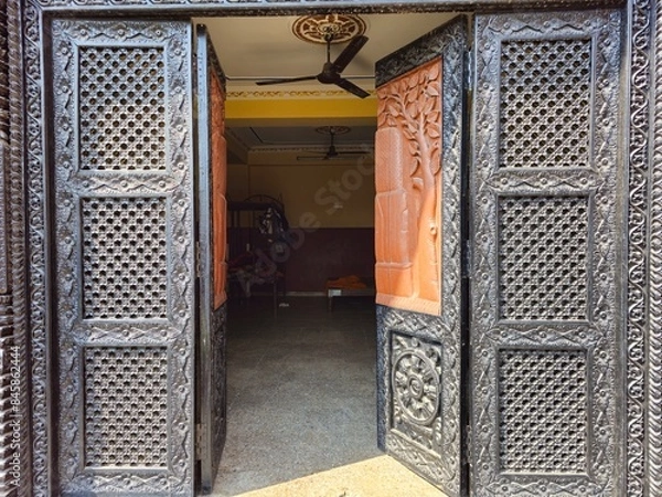 Fototapeta heavy wooden decorated door, open to a dormitory for little Buddhist monks, with warm sunlight cutting across the image. inside visible the bunk beds, a paddle fan on the ceiling