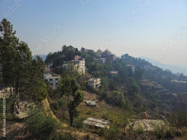 Fototapeta view of the hills of the namo buddha monastery in Nepal, Himalayas, with the guesthouses and the various sections of the temple surrounded by greenery. In the background blue sky with a bit of haze