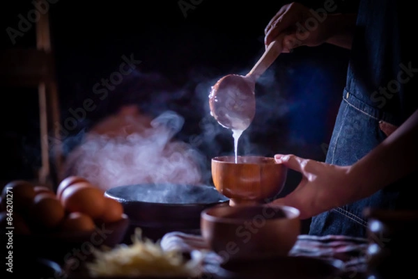 Fototapeta A porridge shop at night on the side of the road as the cook uses a wooden ladle to scoop porridge into a wooden bowl in a retro style. There were eggs and sliced ​​ginger placed on the table.