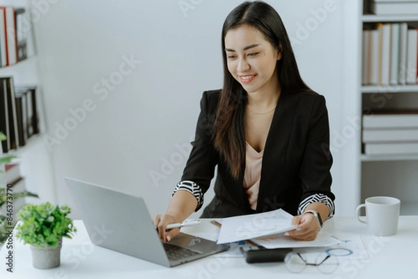 Obraz Asian Businesswoman Using laptop computer and working at office with calculator document on desk, doing planning analyzing the financial report,