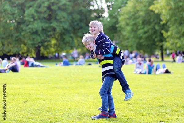Fototapeta Happy kids playing in the park on beautiful summer sunny day. Two school boys, twin brothers, jumping and running together in Hyde park, London, UK. Brotherhood and friendship concept.