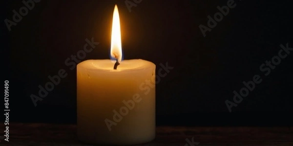 Fototapeta A close-up of a lit candle in the dark, the flame providing a warm light in the darkness