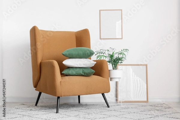 Fototapeta Comfortable armchair with stack of pillows near white wall
