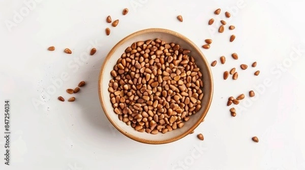 Fototapeta Bowl containing brown pine nuts on a white backdrop