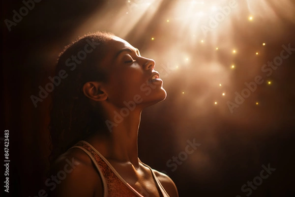 Obraz Woman of faith with eyes closed in prayer is blessed with divine light shining on her face. She looks full of devotion & grace, experiencing the bliss of a mystical experience, a spiritual awakening.