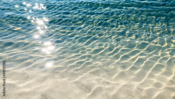 Obraz blue rippled water surface with glittering sun lights at the white sand beach, nature scene background for vacation, travel resort and wellbeing in summertime outdoors