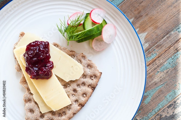 Obraz Scandinavian crisp bread topped with cheese and lingonerry jam served with a salad of cucumber, radish and dill.