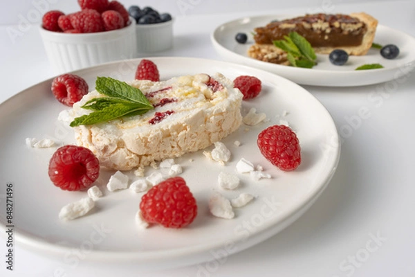 Fototapeta Raspberry meringue roll on a white plate close-up. Dessert on a white background. Breakfast decorated with berries
