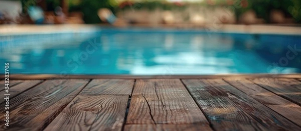 Fototapeta Wooden table in the foreground with a blurry swimming pool in the background