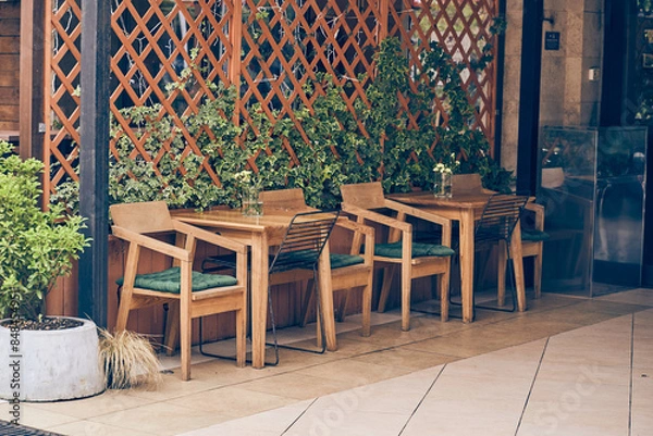 Fototapeta An empty cafe terrace with a wooden table and chair. A cozy street with flowers and a table, facade decor with space to copy. High quality photo