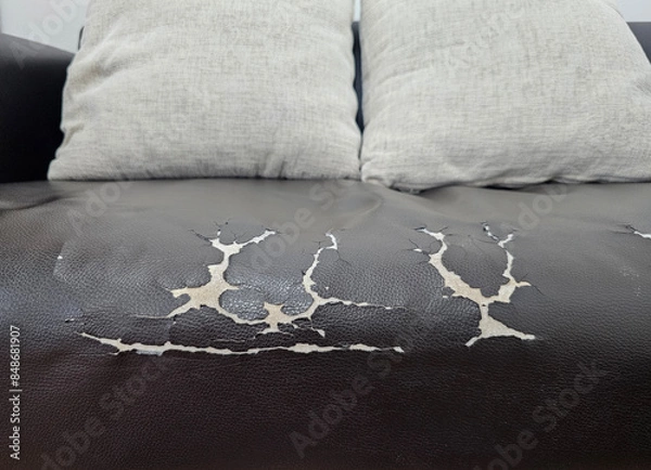 Obraz well worn black leather sofa with visible cracks and peeling, two grey cushions rest on the sofa