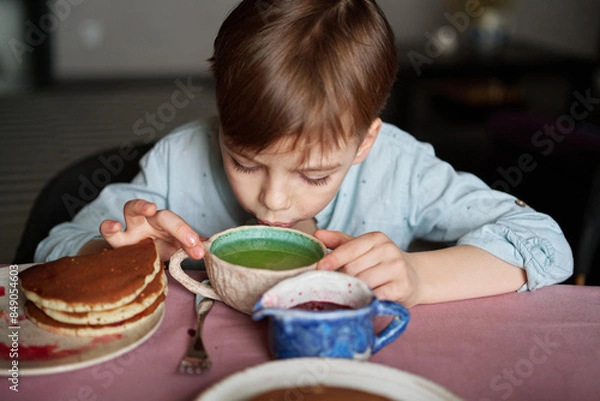 Obraz Little adorable boy drinking tea for breakfast with pancakes and apples at home. Cute weekend with sweet tasty food and emotional child. High quality photo