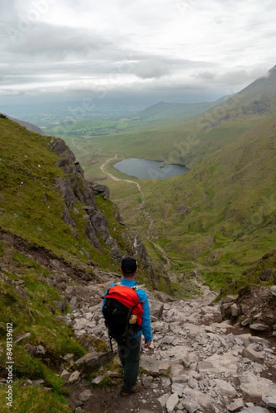 Fototapeta Man is looking towards Devils Ladder, one of most difficult trails, that is leading to highest Irish mountain Carrauntoohill or Carrantuohill is the highest mountain in Ireland at 1038m