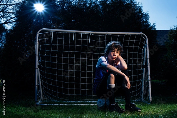 Obraz soccer player sitting in front of the net on his soccer ball