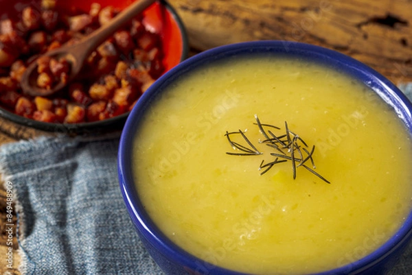 Fototapeta Delicious cassava cream (Caldo ou Creme de Mandioca) or cassava soup, typical of Brazilian cuisine, served in a blue porcelain bowl, on top of a typical rustic farm table, top view with selective focu
