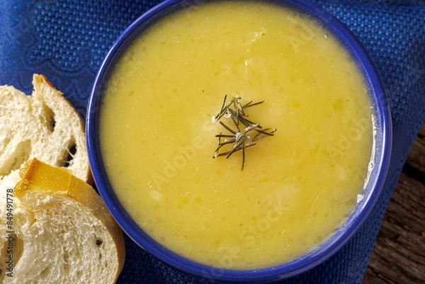Fototapeta Delicious cassava cream (Caldo ou Creme de Mandioca) or cassava soup, typical of Brazilian cuisine, served in a blue porcelain bowl, on top of a typical rustic farm table, top view with selective focu