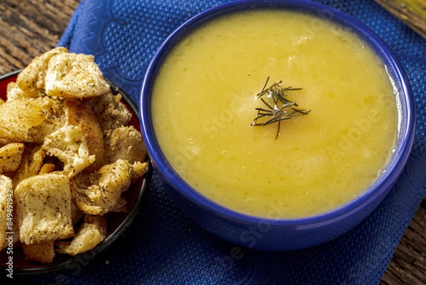 Fototapeta Delicious cassava cream (Caldo ou Creme de Mandioca) or cassava soup, typical of Brazilian cuisine, served in a blue porcelain bowl, on top of a typical rustic farm table, top view with selective focu