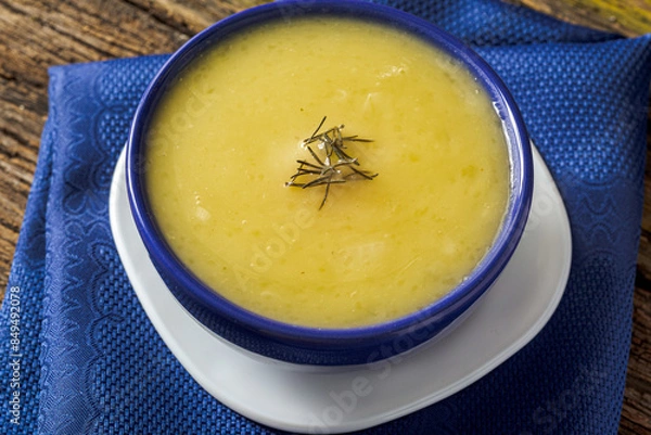 Fototapeta Delicious cassava cream (Caldo ou Creme de Mandioca) or cassava soup, typical of Brazilian cuisine, served in a blue porcelain bowl, on top of a typical rustic farm table, top view with selective focu