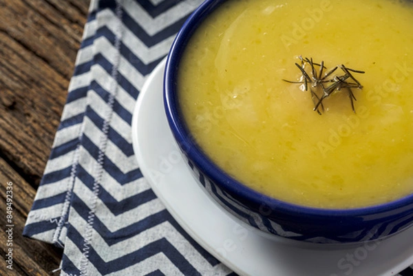 Fototapeta Delicious cassava cream (Caldo ou Creme de Mandioca) or cassava soup, typical of Brazilian cuisine, served in a blue porcelain bowl, on top of a typical rustic farm table, top view with selective focu