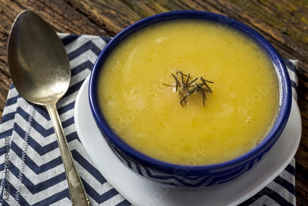 Fototapeta Delicious cassava cream (Caldo ou Creme de Mandioca) or cassava soup, typical of Brazilian cuisine, served in a blue porcelain bowl, on top of a typical rustic farm table, top view with selective focu