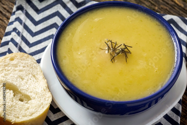 Fototapeta Delicious cassava cream (Caldo ou Creme de Mandioca) or cassava soup, typical of Brazilian cuisine, served in a blue porcelain bowl, on top of a typical rustic farm table, top view with selective focu