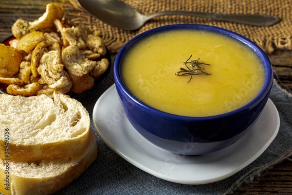 Fototapeta Delicious cassava cream (Caldo ou Creme de Mandioca) or cassava soup, typical of Brazilian cuisine, served in a blue porcelain bowl, on top of a typical rustic farm table, top view with selective focu