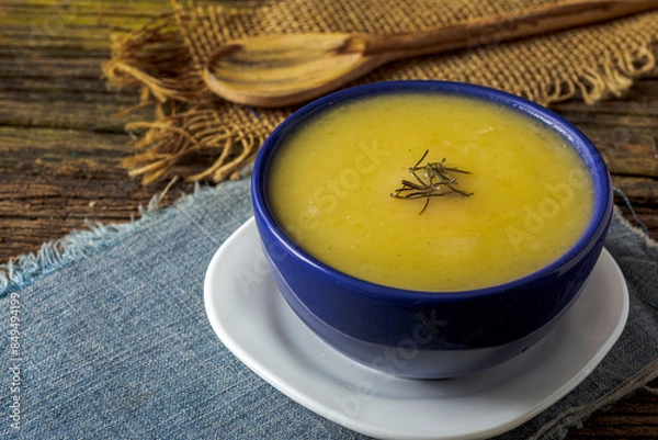 Fototapeta Delicious cassava cream (Caldo ou Creme de Mandioca) or cassava soup, typical of Brazilian cuisine, served in a blue porcelain bowl, on top of a typical rustic farm table, top view with selective focu