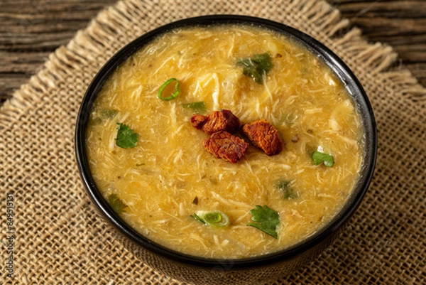 Fototapeta Caldo de Kenga Cassava broth with shredded chicken, typical Brazilian food known as (Caldo de Quenga), in a black pot on top of a rustica with a spoon and slices of bread,  with selective focus