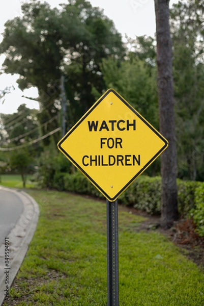Obraz Close-up, crooked, WATCH FOR CHILDREN yellow, diamond sign with space on the left side and tree-lined road and fence in the background, verticle.