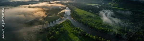 Fototapeta Aerial view of a river flowing through lush green valleys and fields, with fog and clouds adding a magical touch to the scenic landscape.