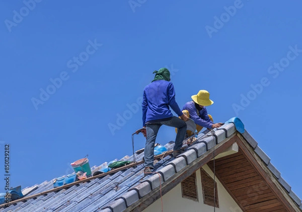 Obraz Repairmans repairing leaking ridges tile roofing and replace cracked broken tile roofing on  blue  sky  background.