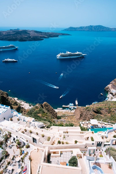 Fototapeta Terraced apartment suites in Fira, with a view towards the Caldera, the volcano island and the tourist packed cruisers