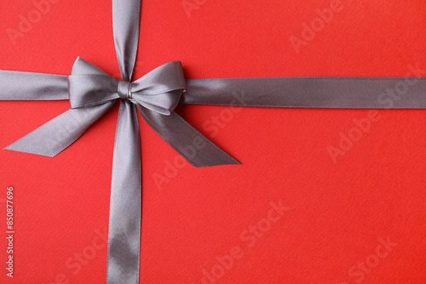 Fototapeta Grey satin ribbon with bow on red background, top view