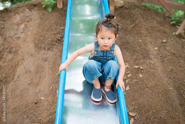 Fototapeta オーバーオールを着て滑り台で遊ぶ女の子