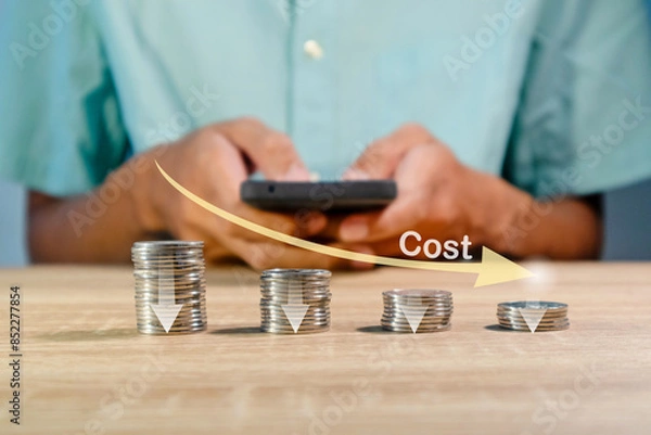 Obraz Coins stacking with the down arrow and man using a smartphone to recalculate the cost. Cost reduction concept.