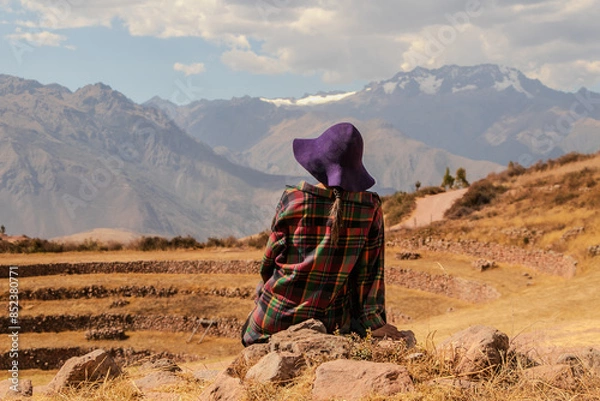 Fototapeta Woman with hat sitting in front of the mountain of Moray in Cusco