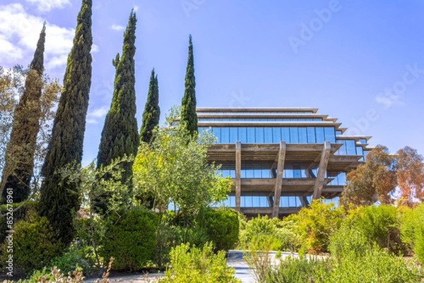 Fototapeta A scenic view of the iconic Geisel Library at UC San Diego, surrounded by lush greenery and tall cypress trees.