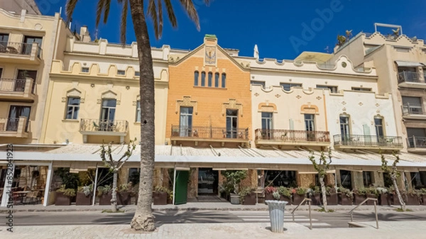 Fototapeta Sunny Mediterranean promenade with charming pastel-colored buildings and palm trees, ideal for travel and holiday-related themes