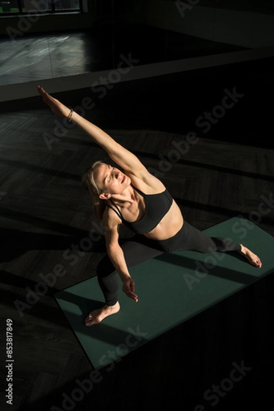 Fototapeta Peaceful young caucasian woman yoga instructor is practicing vinyasa flow, extended side angle yoga ashtanga asana indoors, facing the sunlight with closed eyes. Wellness, lifestyle, copy space.