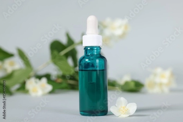Fototapeta Essential oil in bottle and beautiful jasmine flowers on grey background, closeup