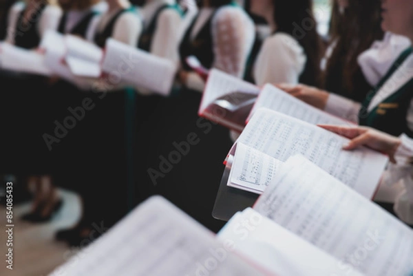 Fototapeta Church choir concert in cathedral, choral artists singing, group of European boys and girls singing in a chorus, students and choristers in white and green uniform performing on stage with conductor