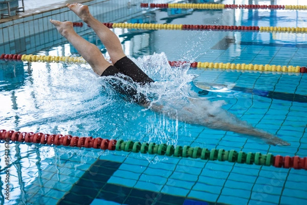 Fototapeta Male swimmer jumping off the starting block into the pool. Concept of determination and competitive sport.