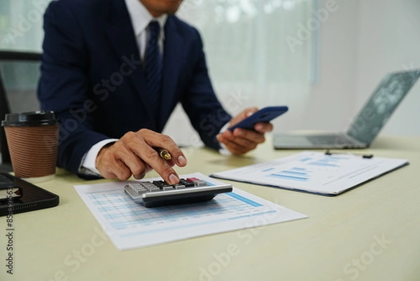 Fototapeta professional businessman is sitting in his office, confidently smiling while working on his laptop. A successful entrepreneur and leader, he embodies corporate success and happiness