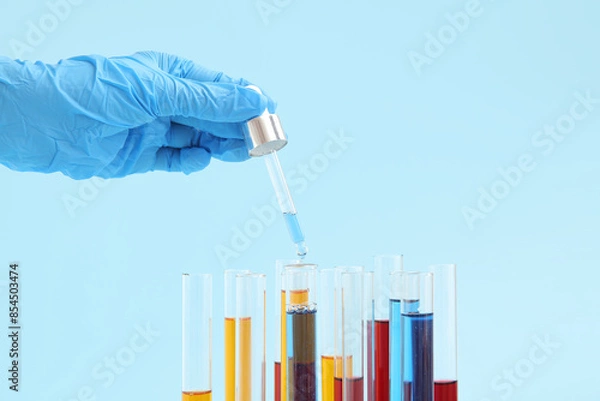 Fototapeta Lab's worker hand with pipette dripping samples into test tubes on blue background