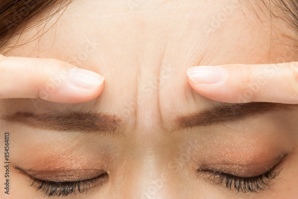 Obraz 女性は眉間のシワを指さしている。