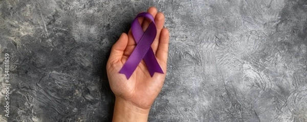Fototapeta Hand holding a purple ribbon symbolizing awareness and support on a textured gray background, representing hope and solidarity.