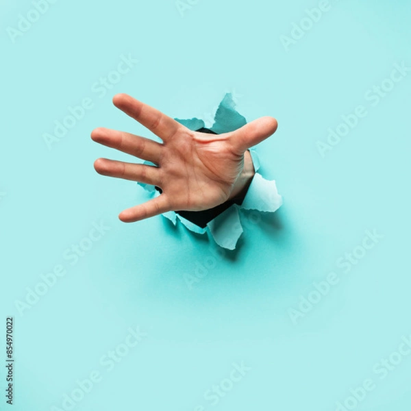 Obraz Hand Bursting through Blue Paper