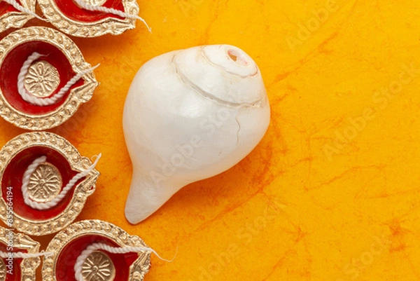 Fototapeta Top view of decorative Diwali Diyas (Earthen oil lamps) with Indian Hindu religious pooja object "Divine Conch" (Shankh in Hindi), on an orange background.