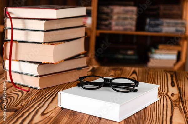 Fototapeta Black glasses lying on a white book next to old books